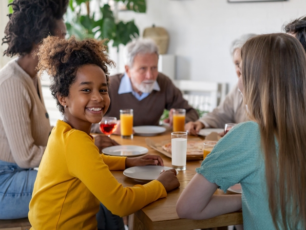 Jeune fille souriant à l'appareil photo alors qu'elle est assise à table avec sa famille.